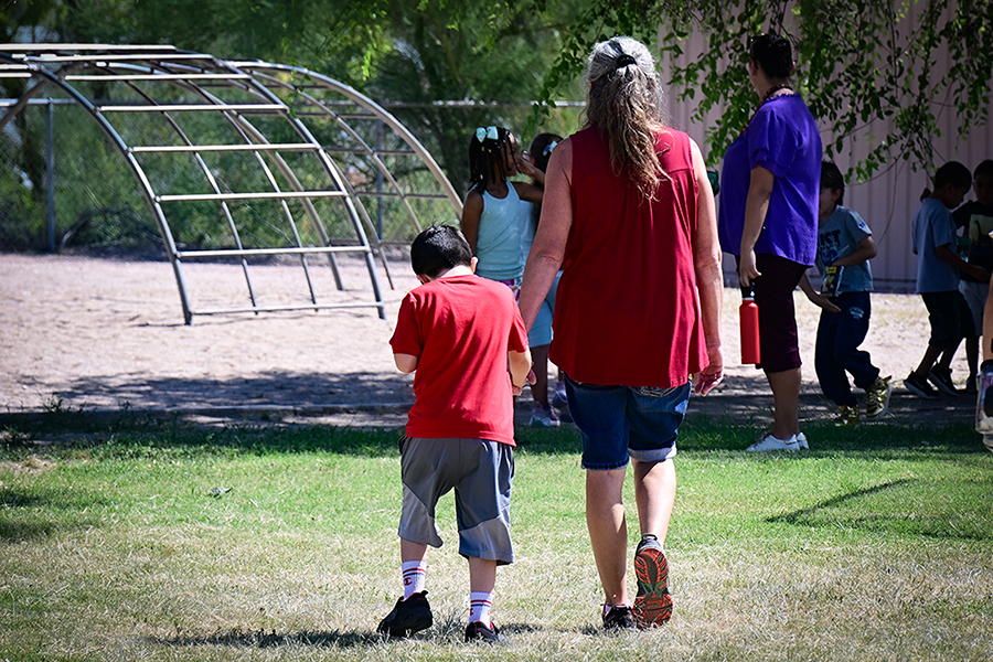 A woman holds a boy's hand by the playground equipment