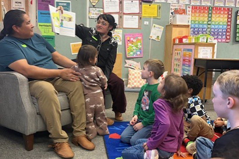 A woman reads from a picture book to a group of students sitting on the floor